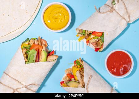 Classique rue nourriture shawarma ou burrito, sandwich sain enveloppé dans la tortilla pain plat avec viande de poulet frite, légumes frais, sauce, sur b vif Banque D'Images