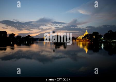 Vue sur le Karaweik (réplique en béton d'une barge royale) et la Pagode Shwedagon de l'autre côté du lac au coucher du soleil, le lac Kandawgyi, Yangon, Myanmar Banque D'Images