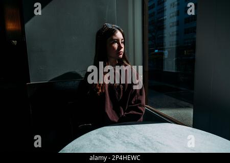 Une jeune fille calme assis dans un café qui regarde par la fenêtre Banque D'Images