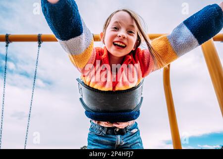 Bonne fille entre jouer sur balançoire le jour ensoleillé Banque D'Images