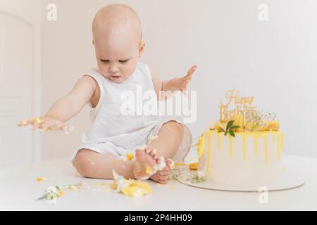 Bébé fille mange son premier gâteau d'anniversaire avec ses mains et ses jambes Banque D'Images