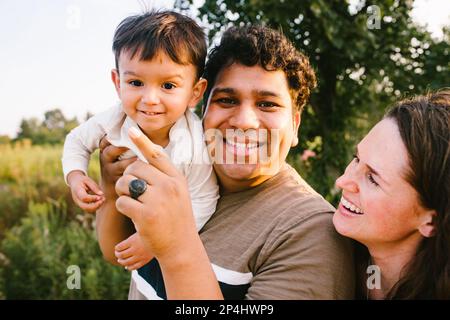 Papa hispanique tient et joue avec son fils tandis que maman rit à l'extérieur Banque D'Images