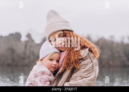 Maman et bébé maussades sont assis dans un parc brumeux près de la rivière qui s'embrasse Banque D'Images