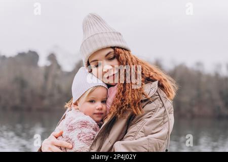 Maman et bébé maussades sont assis dans un parc brumeux près de la rivière qui s'embrasse Banque D'Images