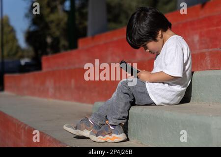 Enfant mexicain jouant avec des appareils mobiles à l'extérieur Banque D'Images