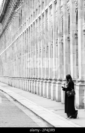 Noir et blanc photo d'une femme seule debout sur fond de colonnes au Palais Royal dans le 1st arrondissement de Paris. Banque D'Images