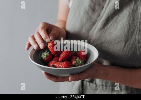 Une assiette en céramique grise avec des fraises dans les mains des femmes. Banque D'Images