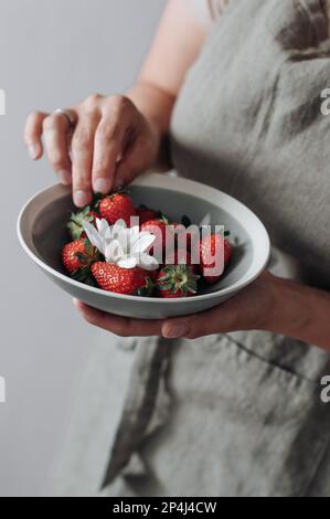 Une assiette grise avec des fraises et des fleurs dans les mains des femmes. Banque D'Images