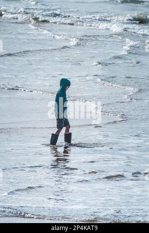 Un jeune garçon portant des bottes Wellington et barbotant dans la mer à Fistral, à Newquay, en Cornouailles, au Royaume-Uni. Banque D'Images