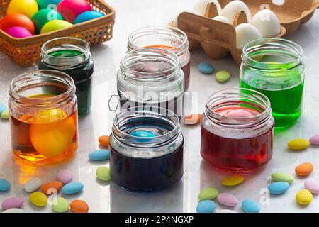 Teindre les œufs de Pâques dans des jarres colorées en verre avec une Candy de Pâques multicolore sur un comptoir en marbre Banque D'Images