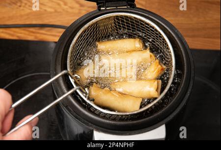 Préparation des rouleaux de ressort dans un pot à frittage spécial. Petits pains cuits dans de l'huile bouillonnante dans la cuisine. Banque D'Images