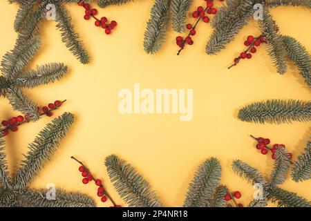 Cadre fait de branches de sapin de nobilis et de baies d'hiver rouges sur fond doré. Concept créatif avec espace de copie. Banque D'Images