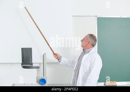 professeur en blouse de laboratoire pointant vers un écran vierge sur le mur Banque D'Images