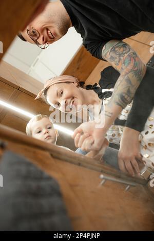 Photo verticale de la femme malonne riante, homme avec manchon tatouage et petit garçon regardant vers le bas à l'appareil photo dans la cuisine Banque D'Images