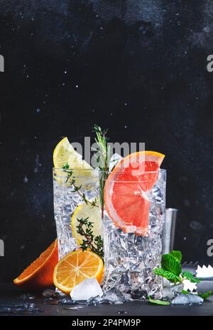 Ensemble de cocktails tonique gin. Boissons alcoolisées à la mode avec citron vert, citron, pamplemousse, orange, concombre, soda et herbes épicées dans des verres à vin, backgroun noir Banque D'Images