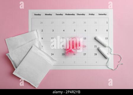 Tapis menstruels, tampons, plumes et calendrier sur fond rose, plat Banque D'Images