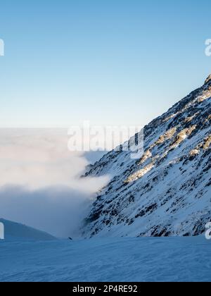 Photo verticale d'une montagne enneigée qui s'élève au-dessus des nuages Banque D'Images