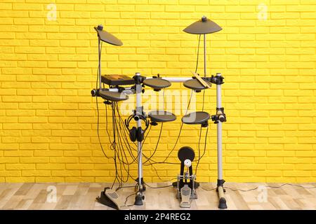 Kit de tambour électronique moderne près du mur de briques jaunes à l'intérieur. Instrument de musique Banque D'Images