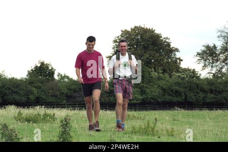 1989, historique, de jour et deux hommes adultes, un père et un fils, en short, t-shirts et bottes, à l'extérieur dans un champ profitant d'une longue marche ou randonnée ensemble, Angleterre, Royaume-Uni. Banque D'Images