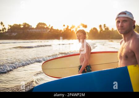 Un jeune garçon avec une planche de surf va à la mer de surf. Il a des vacances d'hiver et profiter d'un beau coucher de soleil avec son père sur l'île du Sri Lanka. Banque D'Images