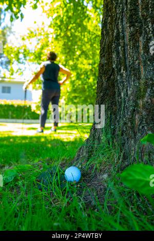 Balle de golf située sur l'herbe rugueuse et golfeur avec Golf Club à la recherche de la balle de golf dans les arbres en une journée ensoleillée en Suisse. Banque D'Images