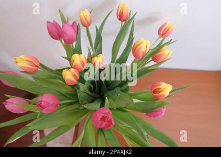 bouquet de tulipes roses et jaunes dans vase vue de dessus sur tiroir en bois et mur blanc. Décoration intérieure. Banque D'Images