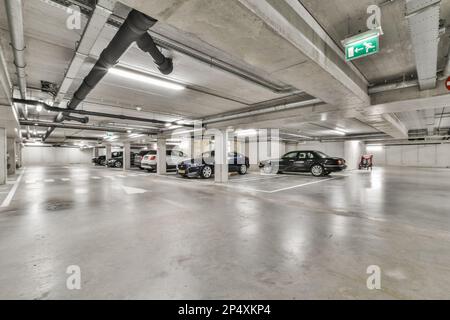 un parking souterrain avec des voitures garées dans l'espace et personne sur le côté droit, il y a un signe vert qui dit Banque D'Images