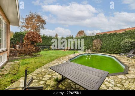 une cour avec une piscine au milieu et de l'herbe verte sur le sol à côté de la piscine est entourée d'arbres Banque D'Images