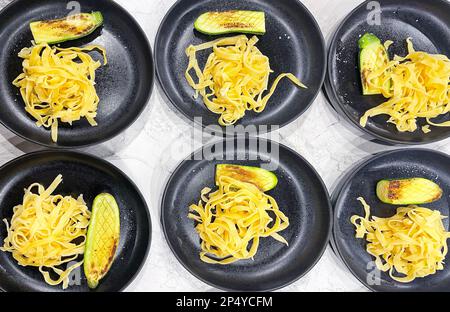 Motif comestible des assiettes noires avec spaghetti. Les assiettes sont des pâtes et des courgettes grillées. Nourriture savoureuse. Arrière-plan de la table en marbre clair. Banque D'Images