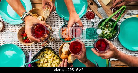 vue au-dessus de la table avec des groupes d'amis qui célèbrent et toaster avec des verres à vin rouge et manger de la nourriture ensemble en s'amusant. Heure du déjeuner an Banque D'Images