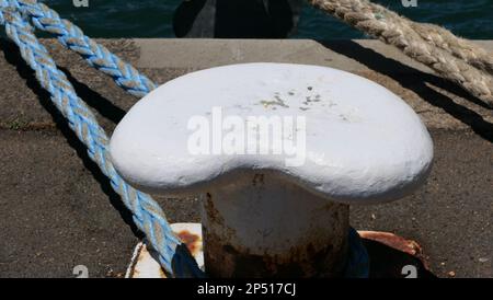 Bollard rouillé de l'harborside avec une corde nautique usée attachée à côté de l'eau Banque D'Images