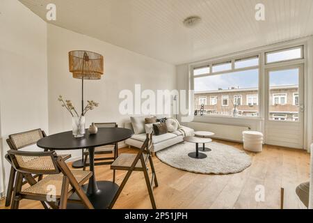 un salon avec murs blancs et parquet, dont une table ronde entourée de deux chaises noires Banque D'Images