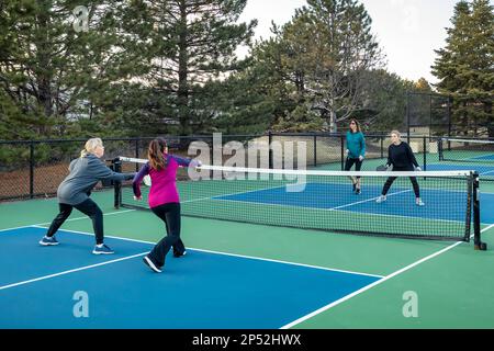 Au début du printemps, quatre joueurs de pickleball de sexe féminin volley près du filet sur un terrain bleu et vert. Banque D'Images