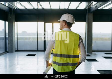 Vue arrière de l'homme en travail gilet debout sur la zone de construction du territoire. Banque D'Images