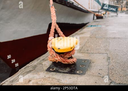 poste d'amarrage en métal jaune avec une corde nouée noire devant l'eau bleue avec un bateau amarré dans un port maritime Banque D'Images