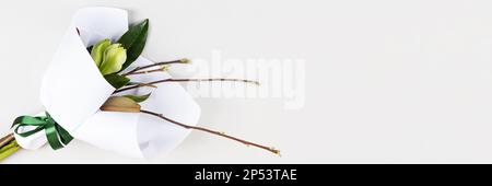 Bouquet de printemps avec branches et feuilles de magnolia et d'amaryllis en papier blanc avec ruban de satin vert sur fond gris. Bonjour printemps. Banque D'Images