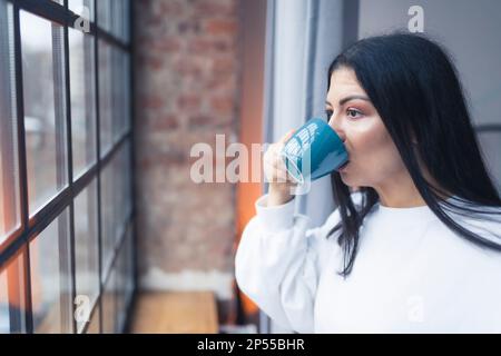 gros plan moyen d'une jeune femme buvant un café et profitant de la vue de la fenêtre. Photo de haute qualité Banque D'Images