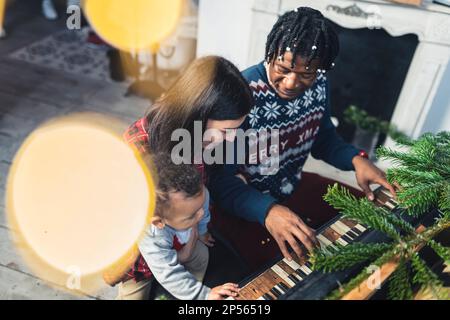 Homme afro-américain jouant sur le piano et sa femme bien-aimée du Caucase et un fils le regardant. Photo de haute qualité Banque D'Images