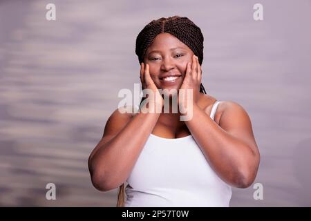 Femme souriante et de taille supérieure faisant un portrait de geste de lavage de visage. Heureuse naturellement belle femme positive corps faisant le traitement du visage et les procédures de soin de peau, posant en studio Banque D'Images