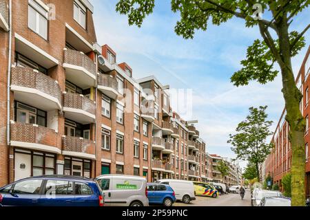 une rue avec des voitures garées sur le côté et des gens qui marchent le long du trottoir devant quelques immeubles d'appartements en briques Banque D'Images