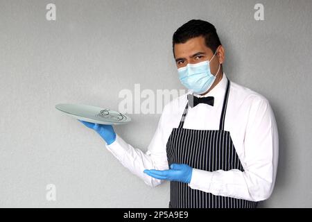 Latino serveur homme avec masque de protection, travaille avec des gants en latex, nouveau normal dans les restaurants. covid-19 Banque D'Images