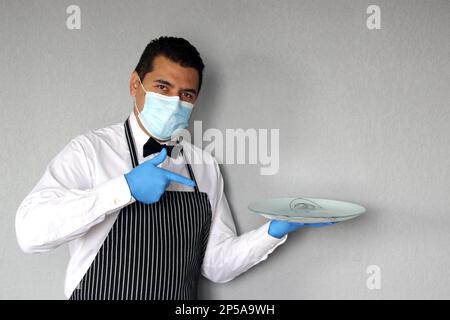 Latino serveur homme avec masque de protection, travaille avec des gants en latex, nouveau normal dans les restaurants. covid-19 Banque D'Images