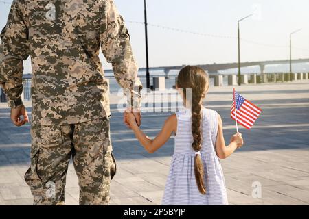 Soldat et sa petite fille avec drapeau américain dehors, vue arrière. Fête des anciens combattants aux États-Unis Banque D'Images