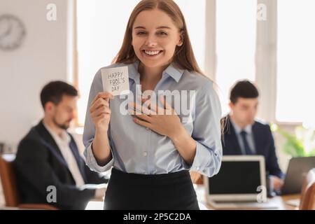 Jeune femme tenant du papier adhésif avec du texte HAPPY FON'S DAY au bureau Banque D'Images