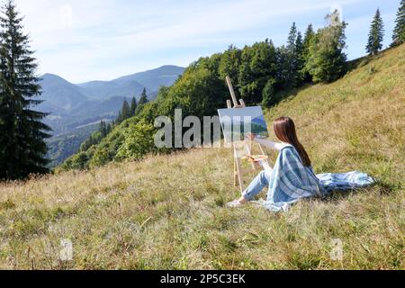 Jeune femme dessin sur chevalet dans les montagnes, vue arrière. Espace pour le texte Banque D'Images