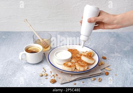 Une femme verse du sirop de caramel sur de savoureuses crêpes au fromage cottage sur une table Banque D'Images