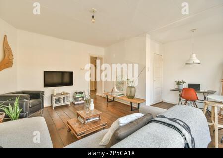 un salon avec murs blancs et parquet, dont un canapé gris et une table basse dans la partie centrale de la chambre Banque D'Images