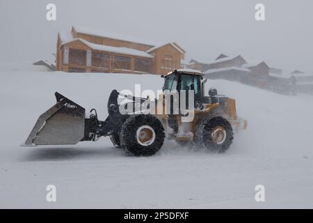 Un tracteur jaune avec chaînes à pneus passe devant une maison en construction lors d'un blizzard à Mammoth Lakes, en Californie. Banque D'Images