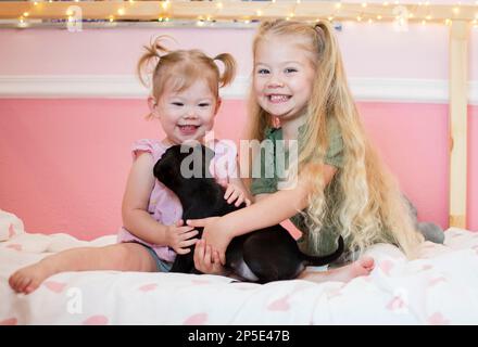 Deux enfants jouant avec un chiot. Enfants avec un animal de compagnie. Des filles heureuses tenant un chien Banque D'Images