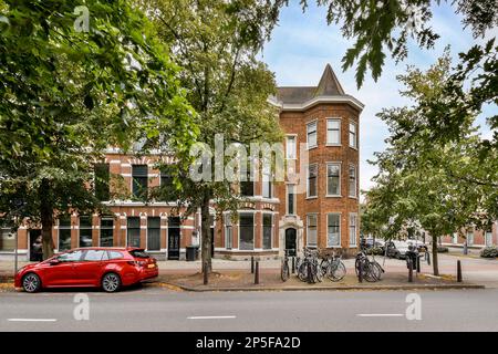 Amsterdam, pays-Bas - 10 avril 2021 : une voiture rouge garée devant un grand bâtiment en briques avec une tour d'horloge sur le dessus et deux bicyclettes attachées à elle Banque D'Images